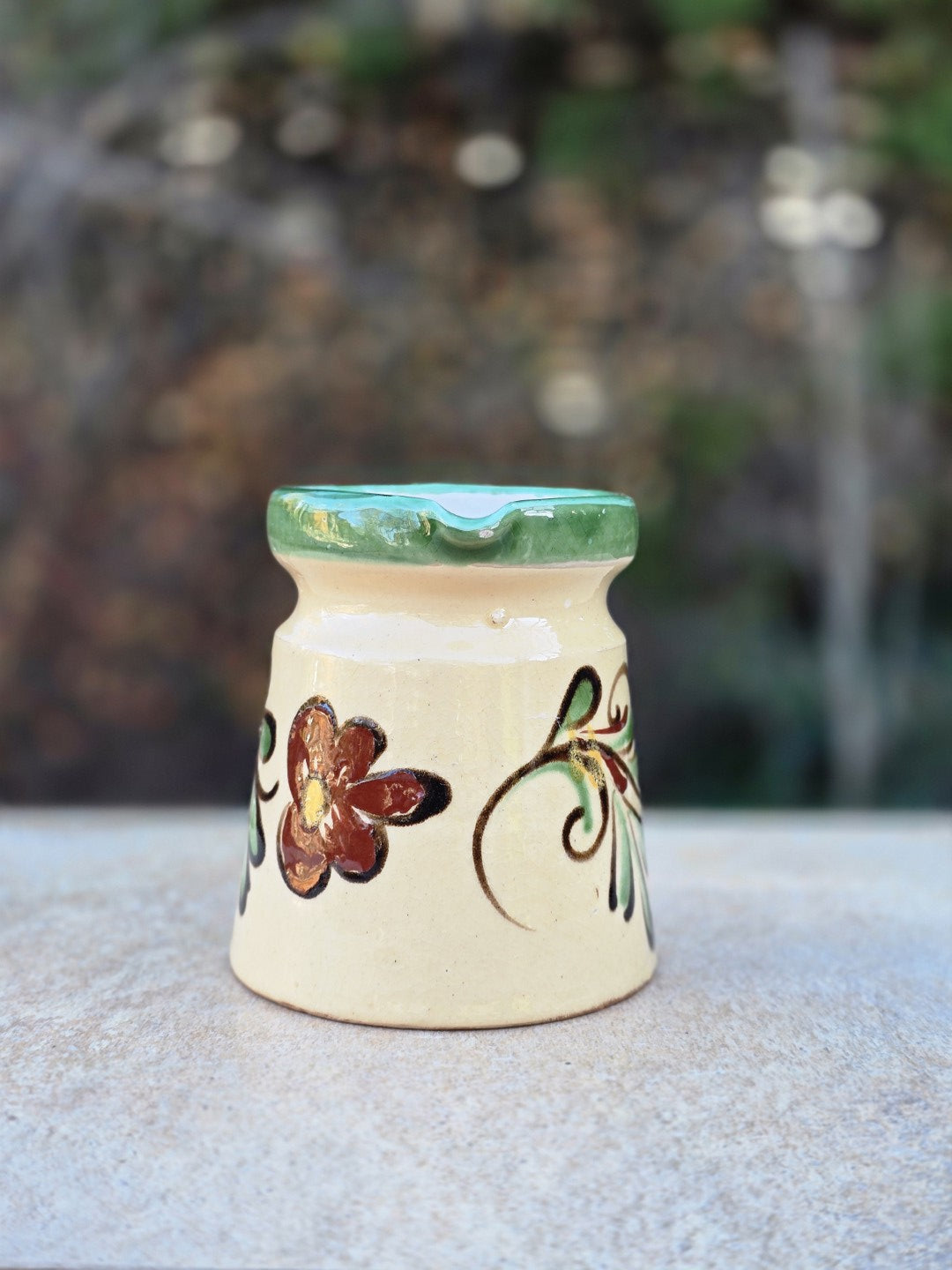 Kleine Vintage-Kanne aus vermutlich ungarischer Majolika mit cremefarbener Glasur, grün abgesetztem Rand, handgemaltem Blumenmotiv und rotscherbigem Boden.