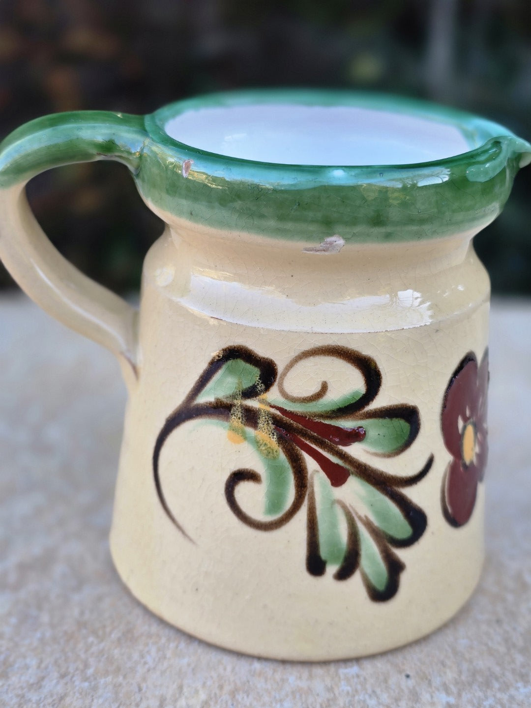 Kleine Vintage Keramikkanne mit handgemalter Blume in Grün und Braun, cremefarbener Glasur, grünem Rand und rotscherbigem Boden.