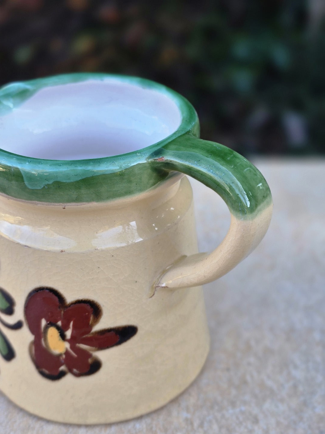 Kleine Vintage-Kanne mit vermutlich ungarischer Majolika-Zuordnung, cremefarbener Glasur, grünem Randdekor, handgemalter Blume und rotscherbigem Boden.