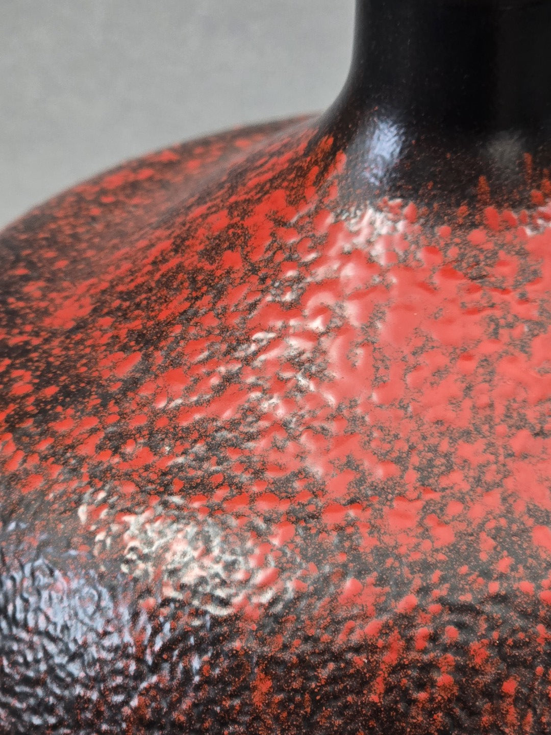 Makroaufnahme der lebendigen rot schwarzen Glasurstruktur auf einer bauchigen Vintage Vase