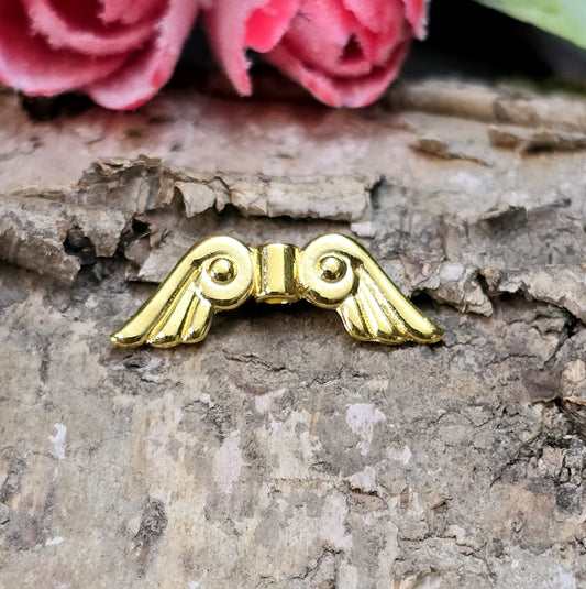 Das Bild zeigt vergoldete Metallperlen in Form von Engelsflügeln. Die Perlen sind 22 mm lang und zeichnen sich durch zarte, filigrane Details aus, die den Flügeln eine elegante und anmutige Erscheinung verleihen.