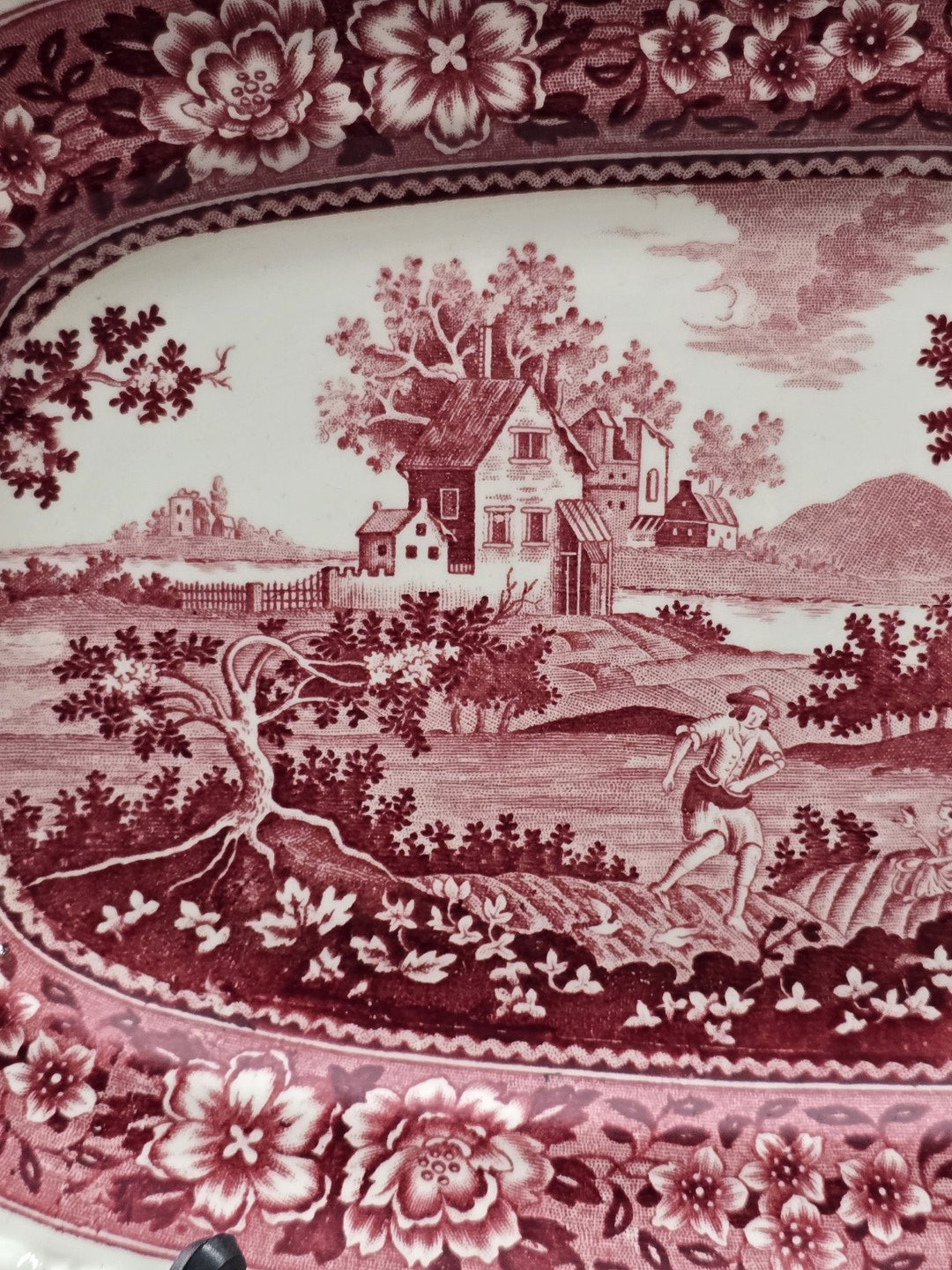 Vintage Rusticana Servierplatte mit ländlichem Gehöft, arbeitender Figur und roter Blütenbordüre in dekorativer Nahaufnahme