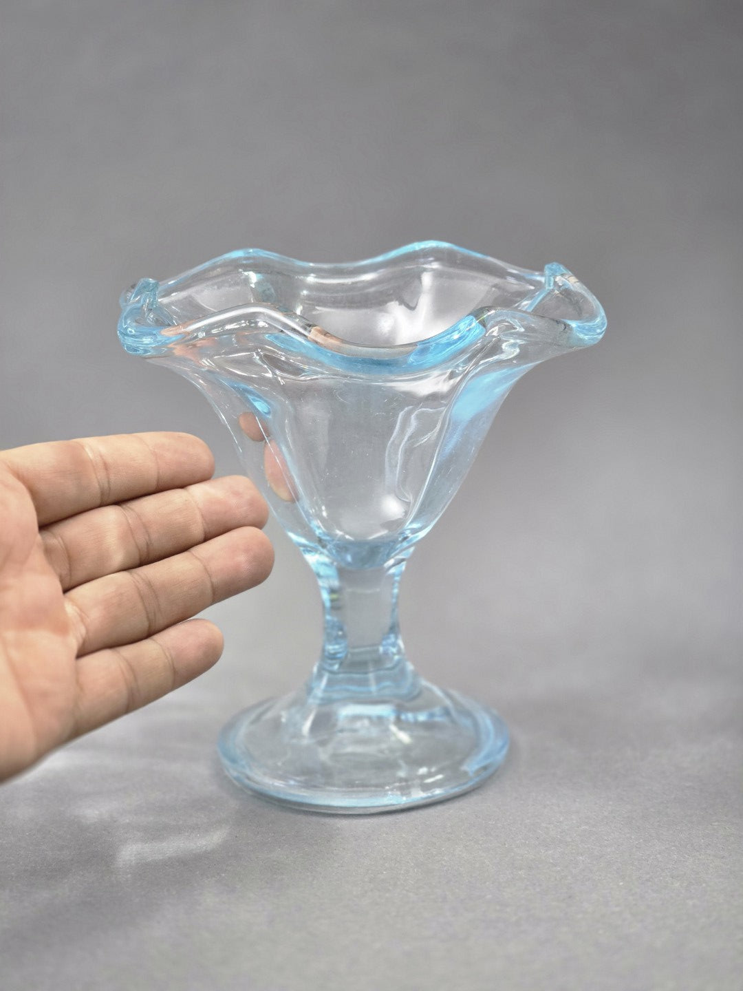 Eine Hand neben dem Glas zeigt die Größe des Eisbechers; gut sichtbar sind die breite Schale, der kurze Stiel und der wellige Rand.