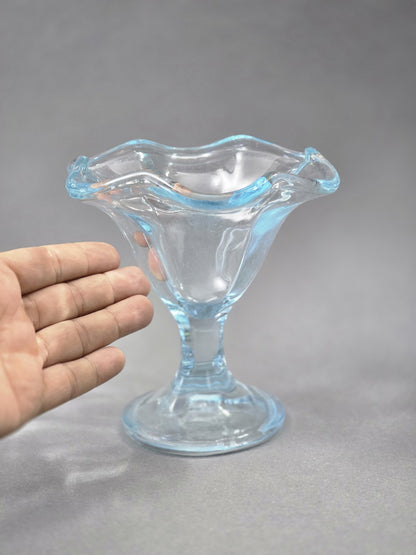 Eine Hand neben dem Glas zeigt die Größe des Eisbechers; gut sichtbar sind die breite Schale, der kurze Stiel und der wellige Rand.