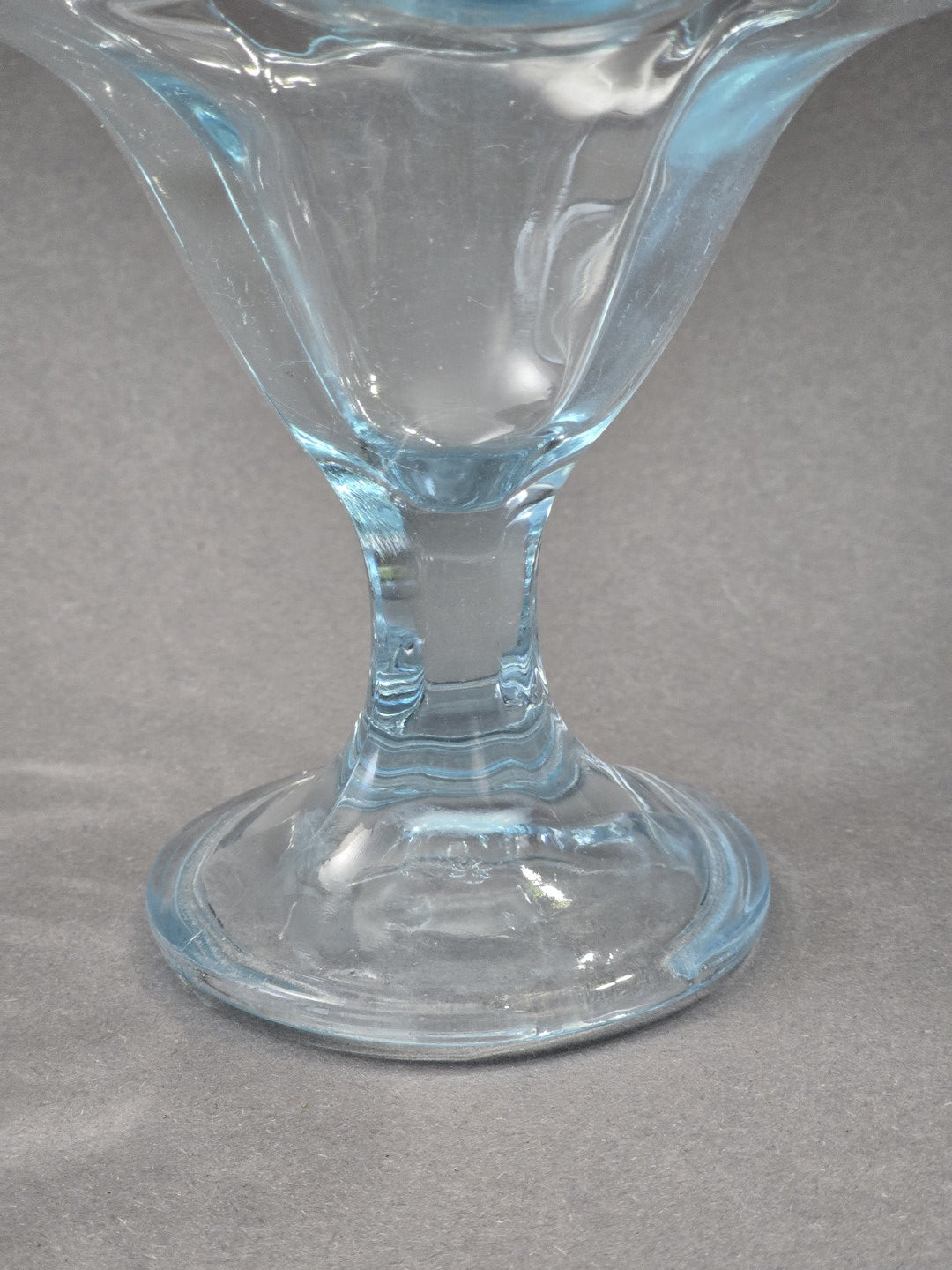 Detail von Stiel und Standfuß des Eisbechers, das Glas ist transparent mit zartblauem Schimmer und wirkt fest gepresst.