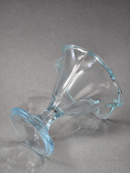 Der Eisbecher liegt seitlich auf dem grauen Untergrund, sodass Fuß, Stiel, Schale und der geschwungene Rand vollständig sichtbar sind.