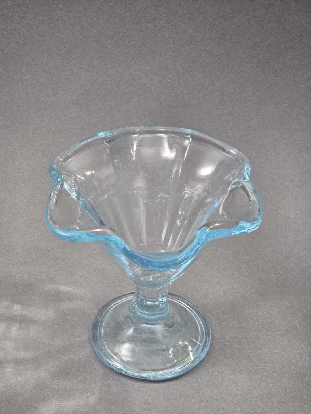Blick von oben in den Eisbecher, der Rand bildet eine weiche Wellenform und das transparente Glas zeigt einen kühlen blauen Schimmer.