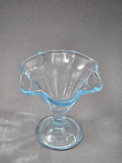 Blick von oben in den Eisbecher, der Rand bildet eine weiche Wellenform und das transparente Glas zeigt einen kühlen blauen Schimmer.