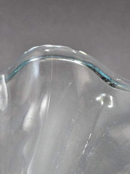 Nahaufnahme des gewellten Glasrands mit hellblauer Tönung, glänzender Oberfläche und kleinen sichtbaren Spuren im transparenten Glas.