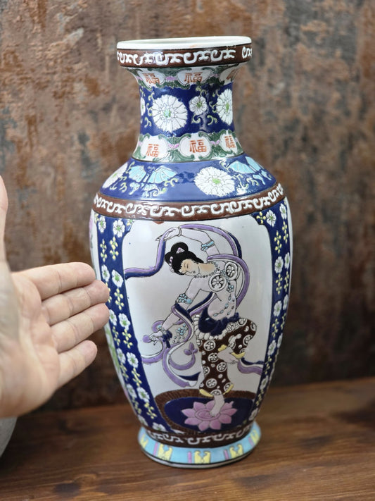 Vintage Porzellanvase mit figürlicher Tänzerin und blau-weißem Dekor neben einer Hand zur Veranschaulichung der Größe.