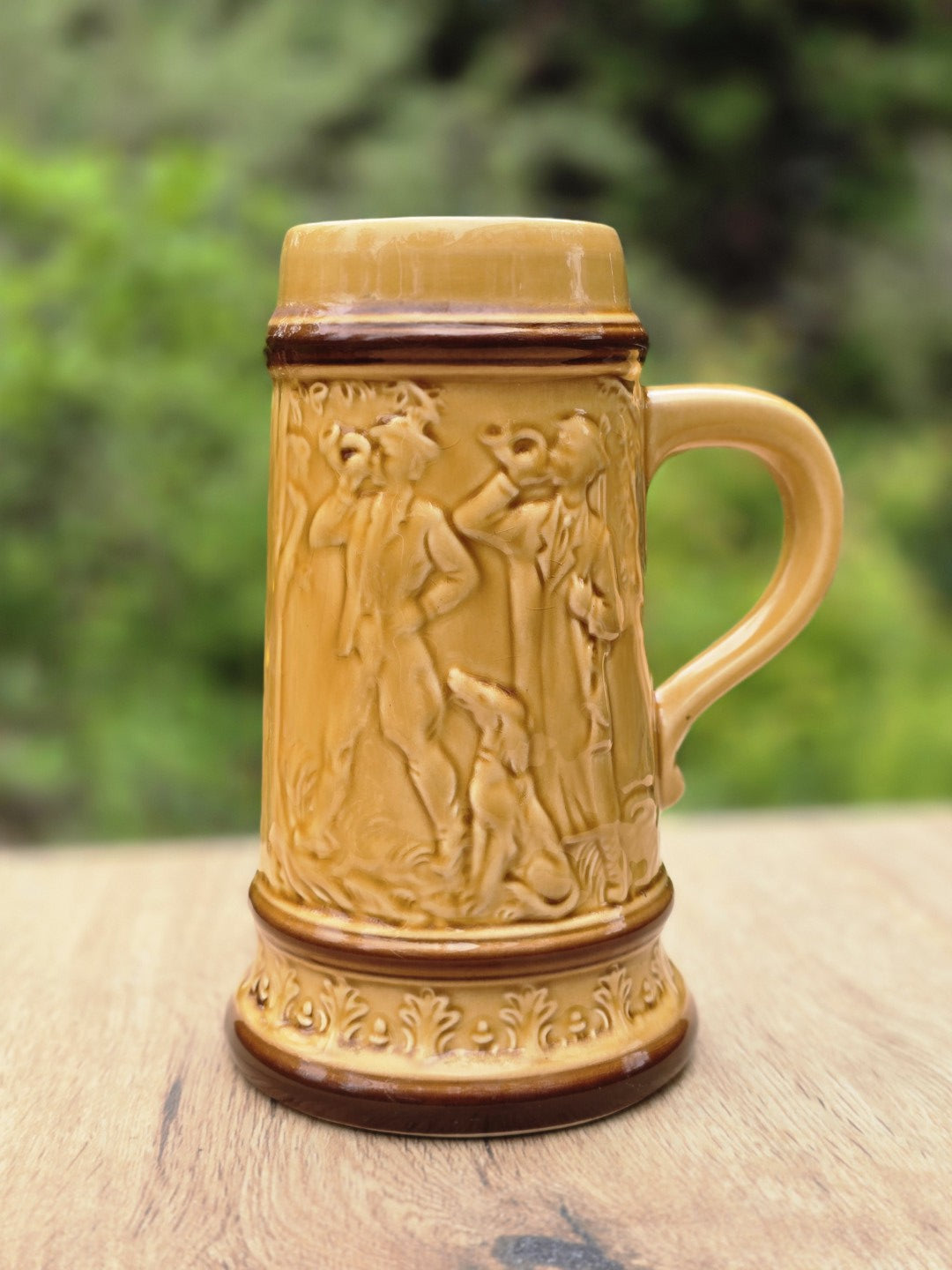 Frontalansicht eines honiggelben Vintage Bierkrugs aus Keramik mit braunen Rändern, Jagdrelief, Figuren, Hund und Ornamentdekor