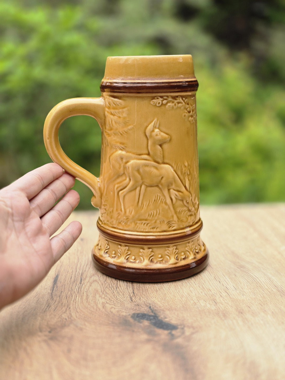 Seitliche Ansicht des Keramik Bierkrugs mit Henkel, Hirschrelief, honigbrauner Glasur und Hand zum Größenvergleich