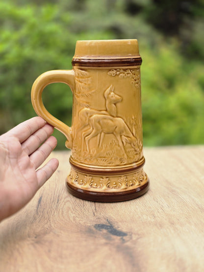 Seitliche Ansicht des Keramik Bierkrugs mit Henkel, Hirschrelief, honigbrauner Glasur und Hand zum Größenvergleich