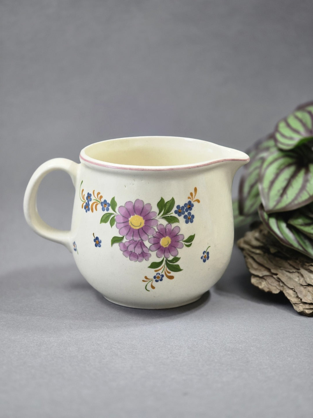Frontansicht des floralen Milchkännchens mit geschwungener Gießnase, Henkel und rosa-blauem Blumendekor auf hellem Grund
