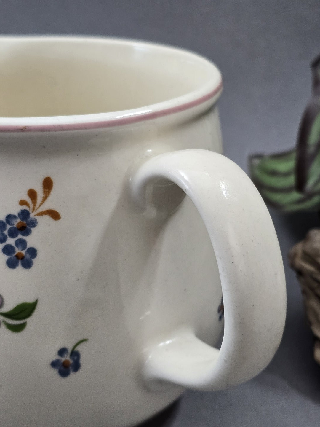 Detailansicht des weißen Henkels mit glatter Glasur, rosa Randlinie und kleinem blauem Blütendekor