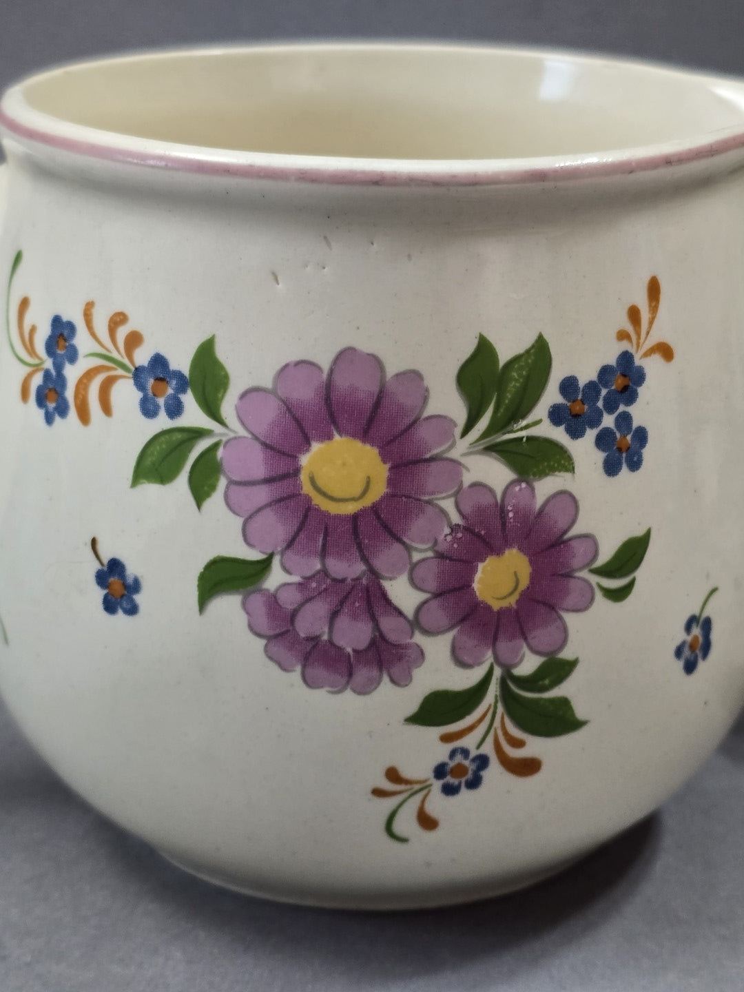 Florales Detail mit rosa Blüten, blauen kleinen Blumen und grünen Blättern auf cremefarbener Vintage-Keramik