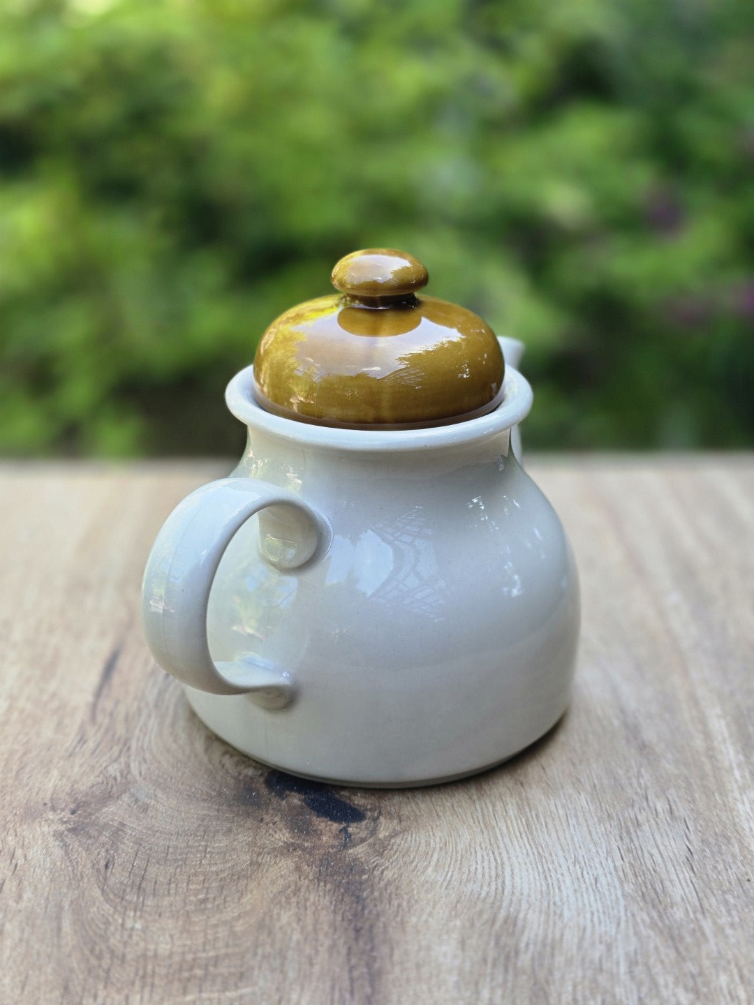 Vintage Teekanne von hinten mit hellem Korpus, olivgrünem Deckel und glänzender Glasur.
