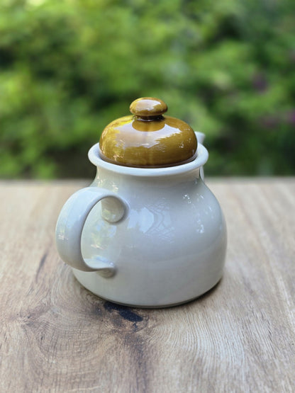 Vintage Teekanne von hinten mit hellem Korpus, olivgrünem Deckel und glänzender Glasur.