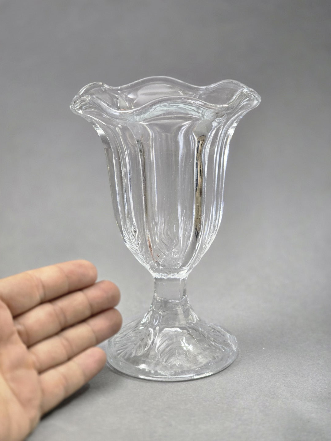 Der Glasbecher ist von vorn zu sehen, mit hohen senkrechten Glasrippen, tulpenförmiger Öffnung und dekorativ geformtem Fuß