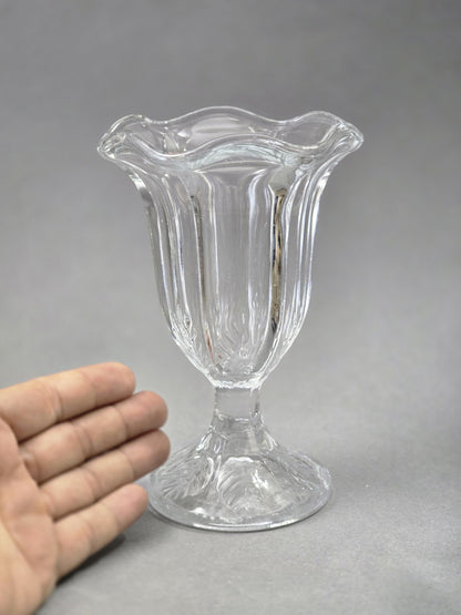 Der Glasbecher ist von vorn zu sehen, mit hohen senkrechten Glasrippen, tulpenförmiger Öffnung und dekorativ geformtem Fuß