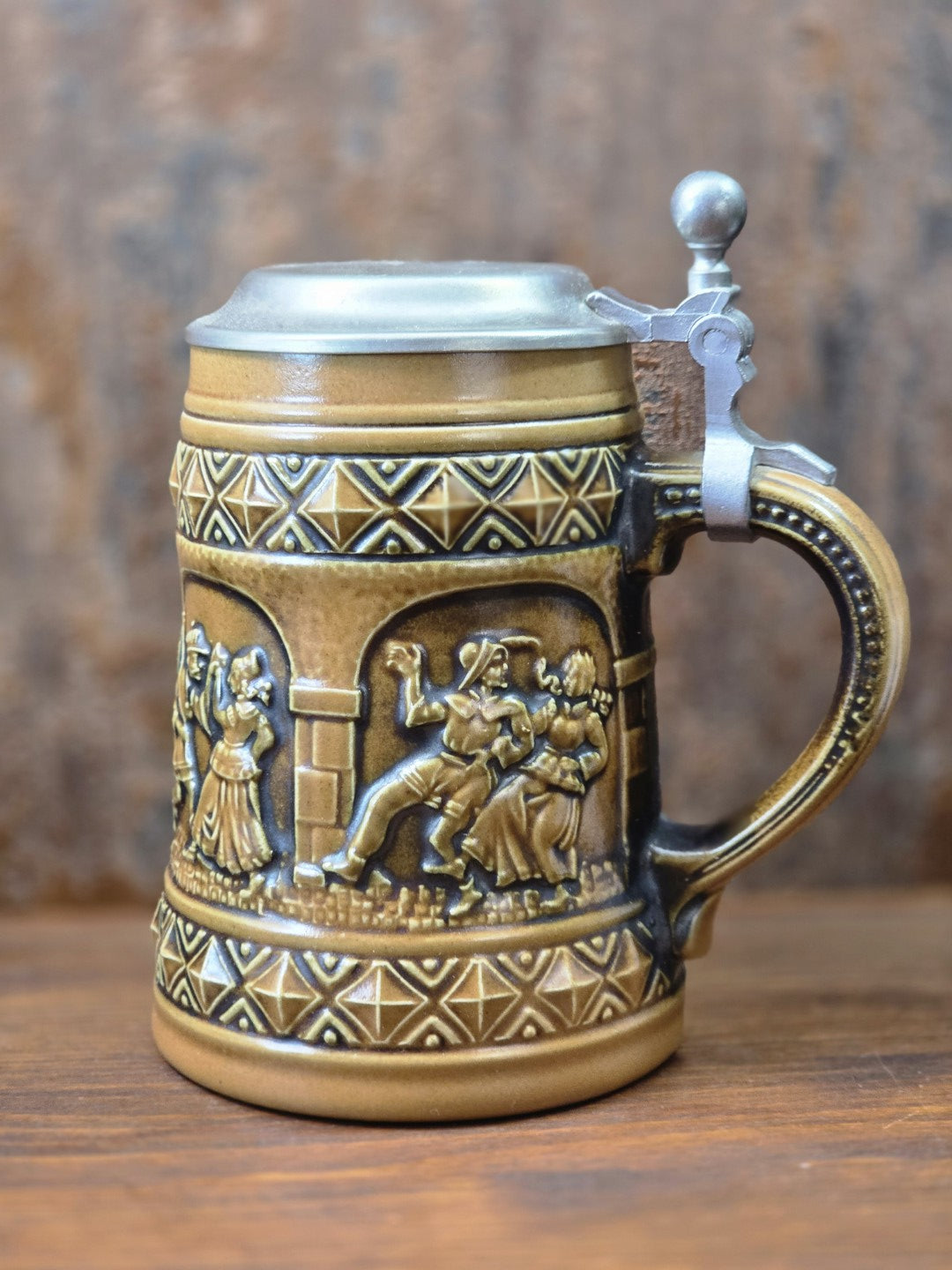 Vintage Steinzeug-Bierkrug von Gerzit mit braunem Henkel, Zinndeckel und reliefierter Tanzszene zwischen geometrischen Dekorbändern.