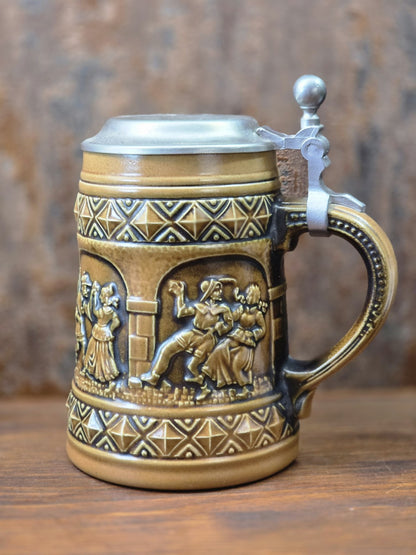 Vintage Steinzeug-Bierkrug von Gerzit mit braunem Henkel, Zinndeckel und reliefierter Tanzszene zwischen geometrischen Dekorbändern.