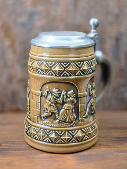 Vintage Gerzit Bierkrug mit Zinndeckel und reliefiertem Tanzpaar unter einer Arkade, dazu braun-schwarzes geometrisches Randdekor.