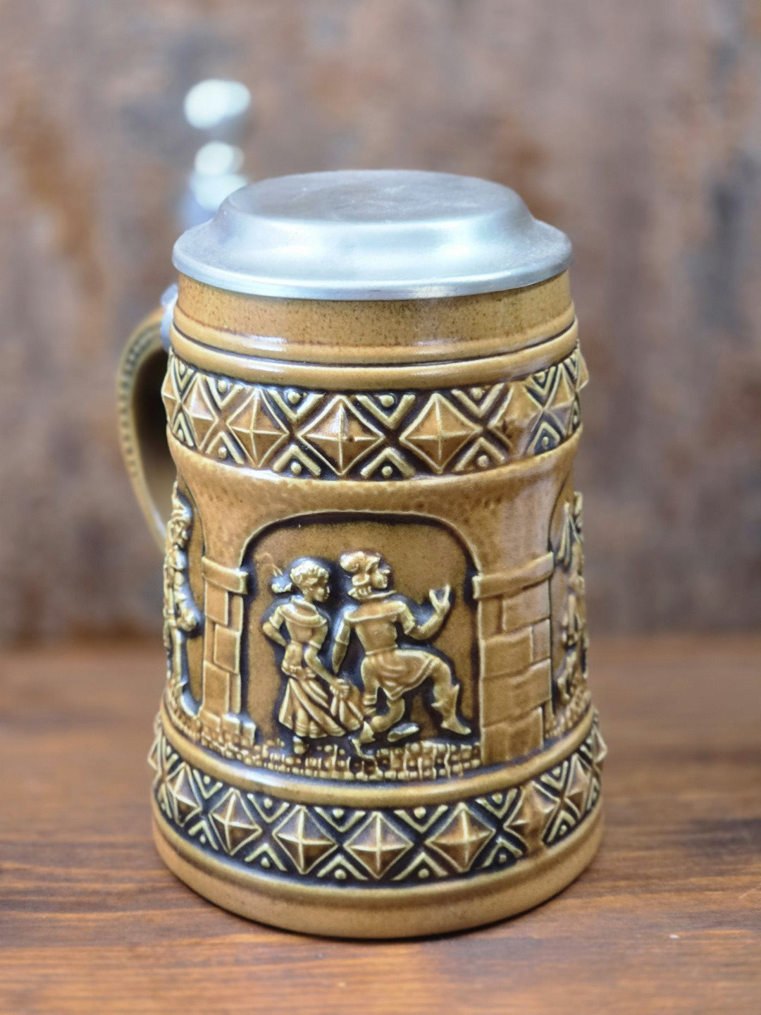Vintage Gerzit Bierkrug aus braunem Steinzeug mit Zinndeckel und Reliefszene eines tanzenden Paares in rückwärtiger Ansicht.