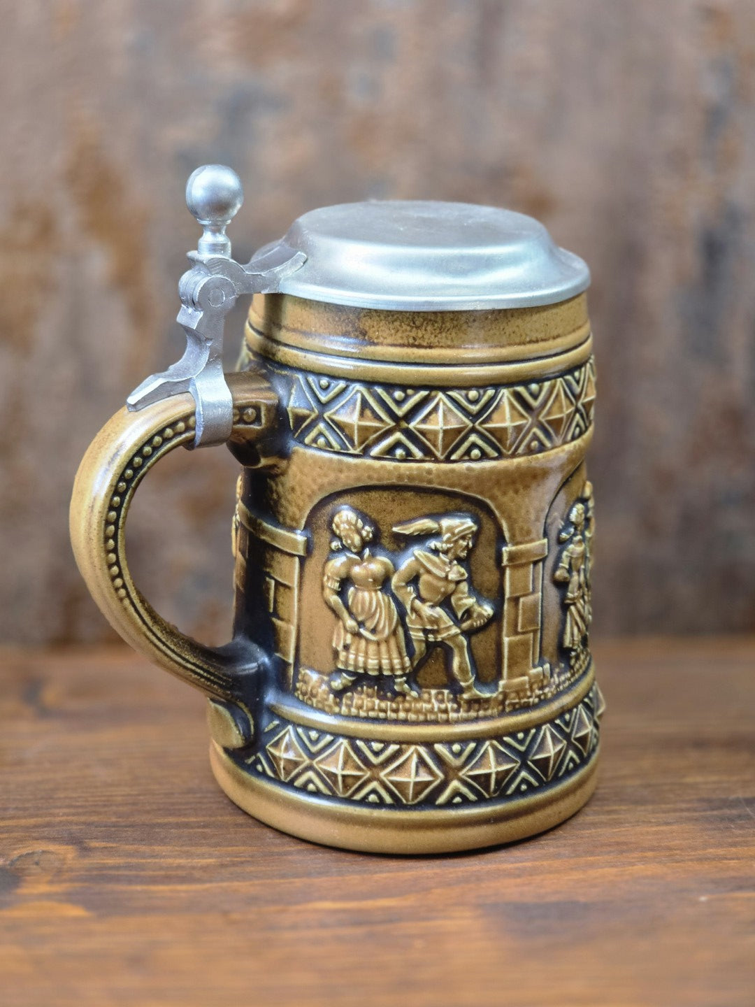 Vintage Steinzeug-Bierkrug von Gerzit mit Zinndeckel, Henkel und plastischem Paarrelief unter einer Arkade in Seitenansicht.