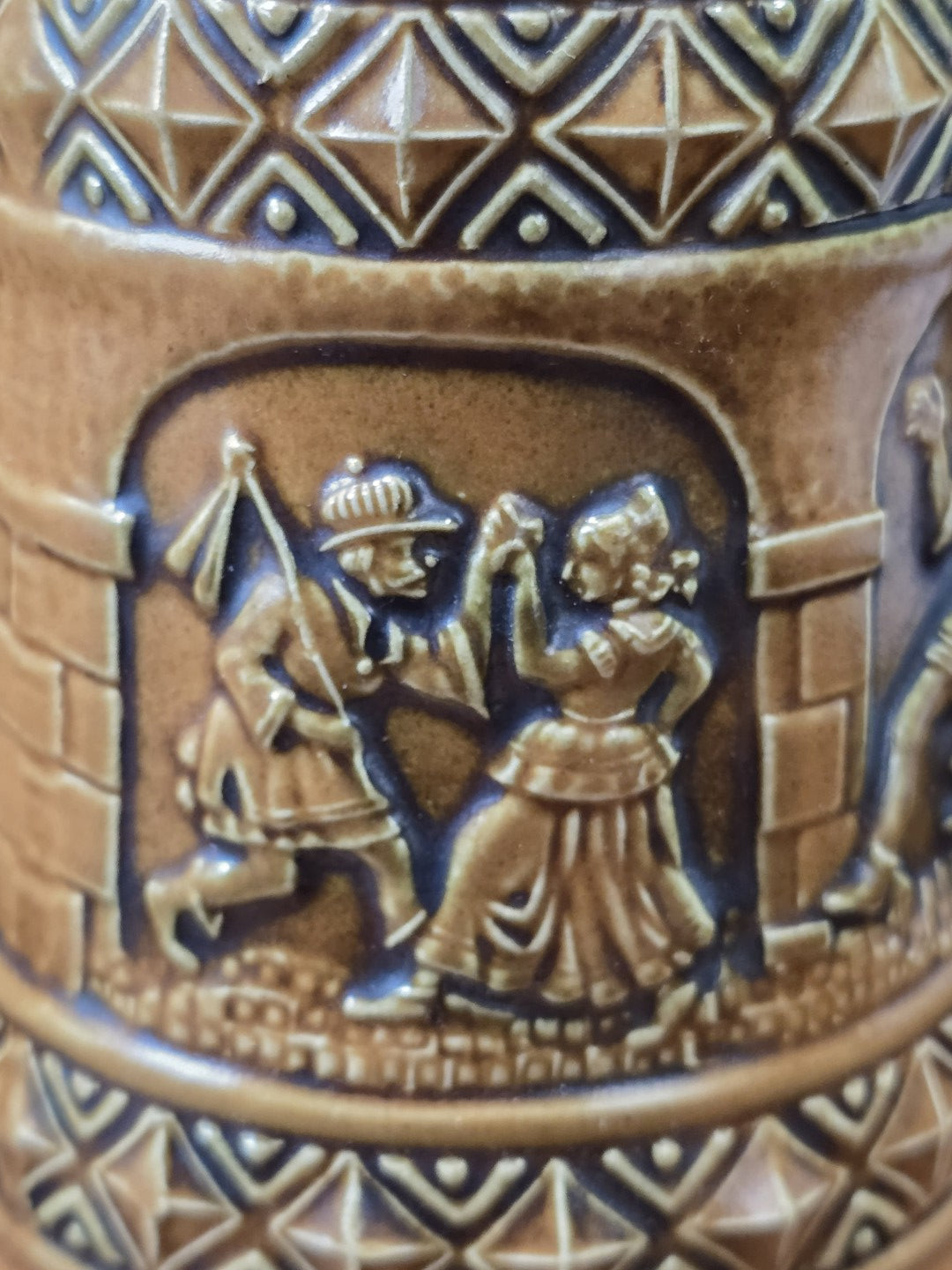 Vintage Gerzit Bierkrug mit plastischem Relief eines tanzenden Paares unter einer Arkade und geometrischem Dekor in Nahaufnahme.