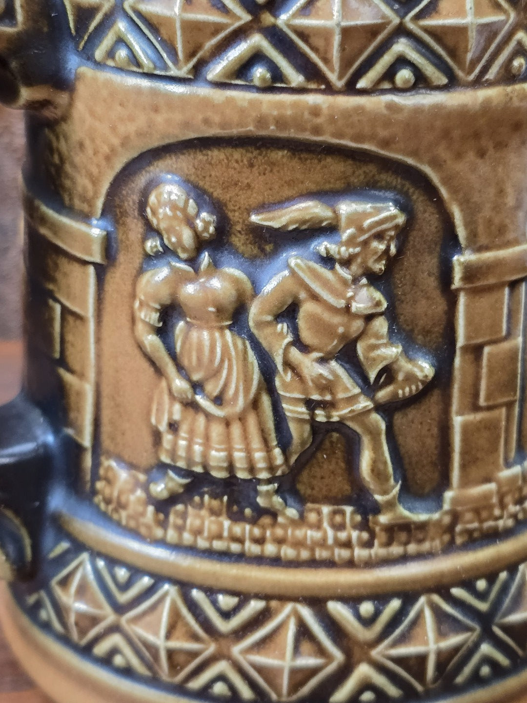 Vintage Gerzit Bierkrug mit plastischem Figurenrelief eines Paares, brauner Glasur und geometrischem Dekorband in Nahaufnahme.