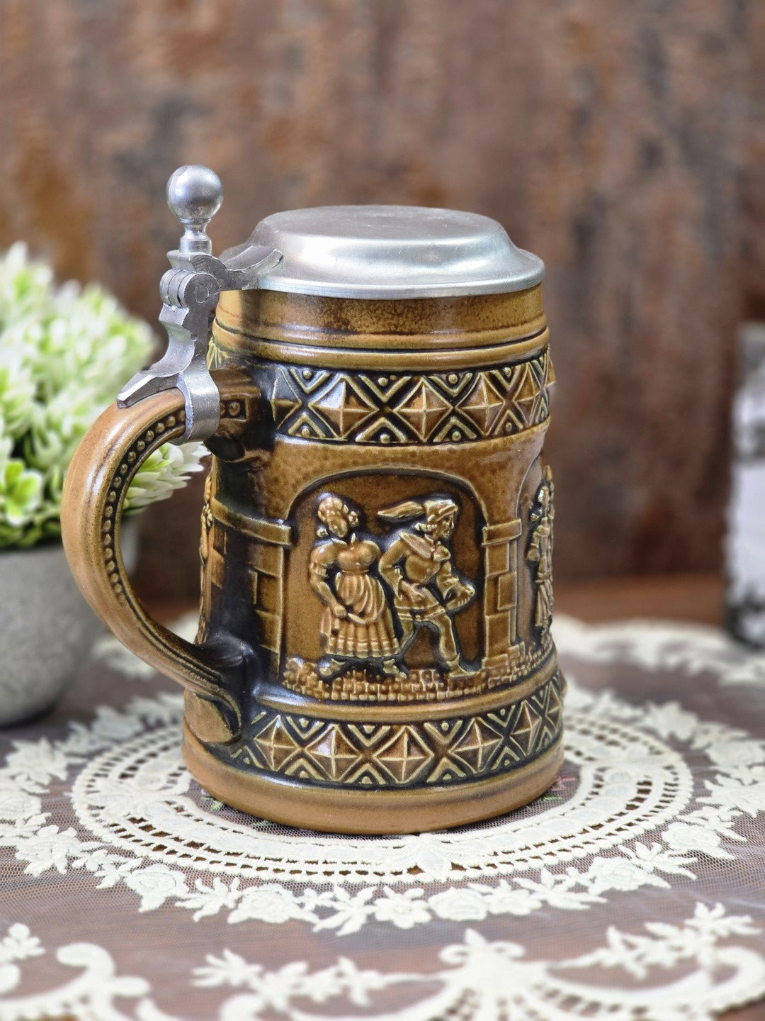 Vintage Steinzeug-Bierkrug von Gerzit mit Zinndeckel, braunem Henkel und plastischem Paarrelief in schräger Seitenansicht.