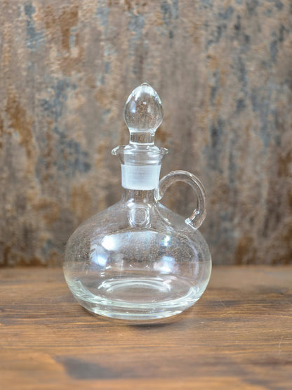 Vintage Glasdekanter mit Stöpsel, rundem Korpus, seitlichem Henkel und klarem Glas auf Holztisch