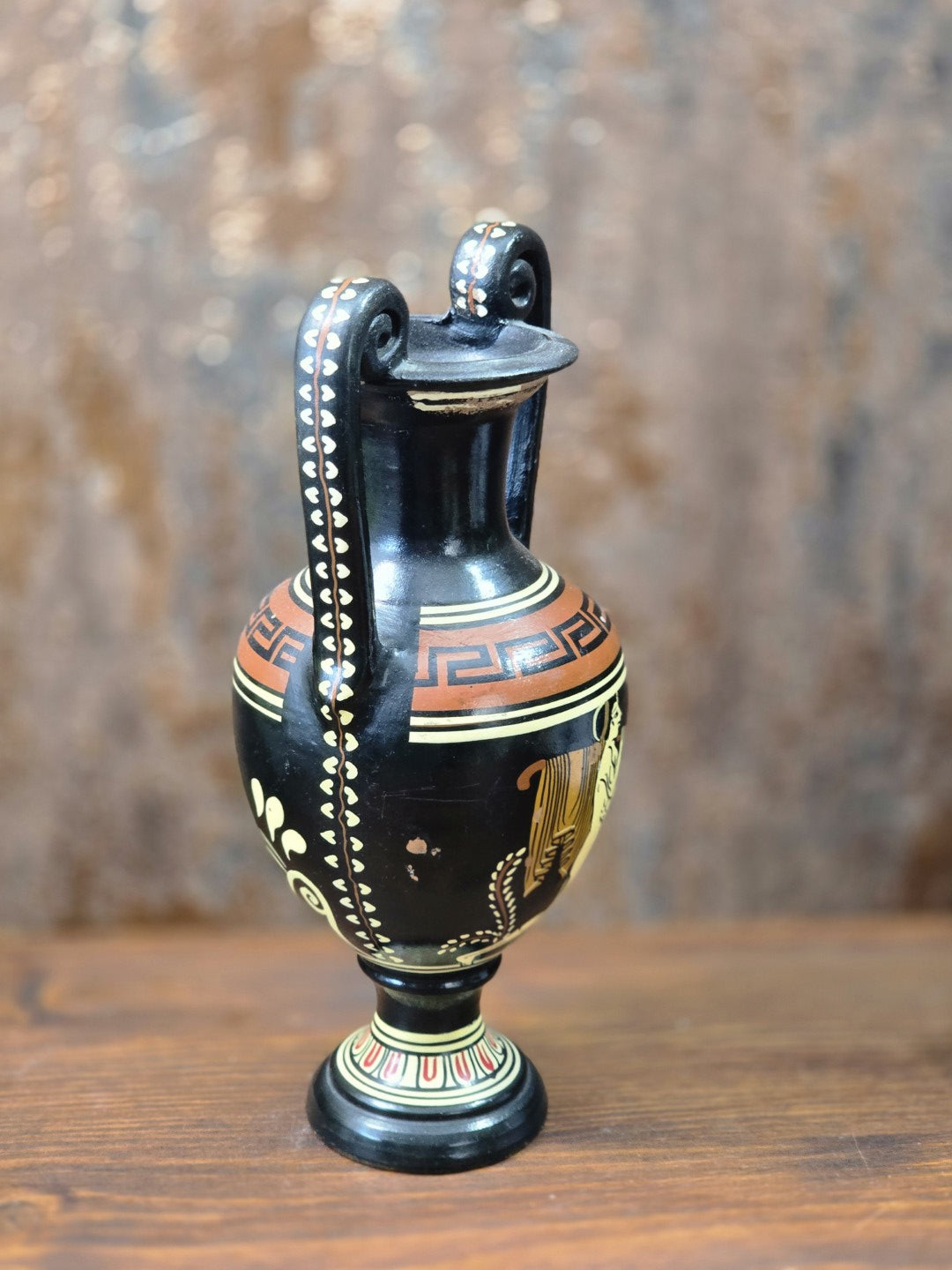 Griechische Keramikamphora mit schwarzer Oberfläche, bemaltem Mäanderband und dekorierten Volutenhenkeln in seitlicher Ansicht