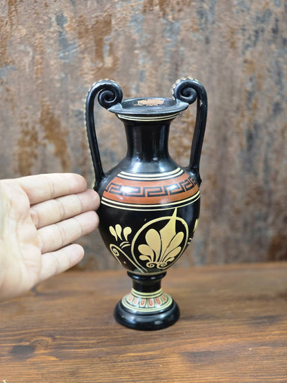 Vintage Keramikamphora mit schwarzem Grund und Palmettenmotiv neben einer Hand als Größenvergleich auf Holztisch