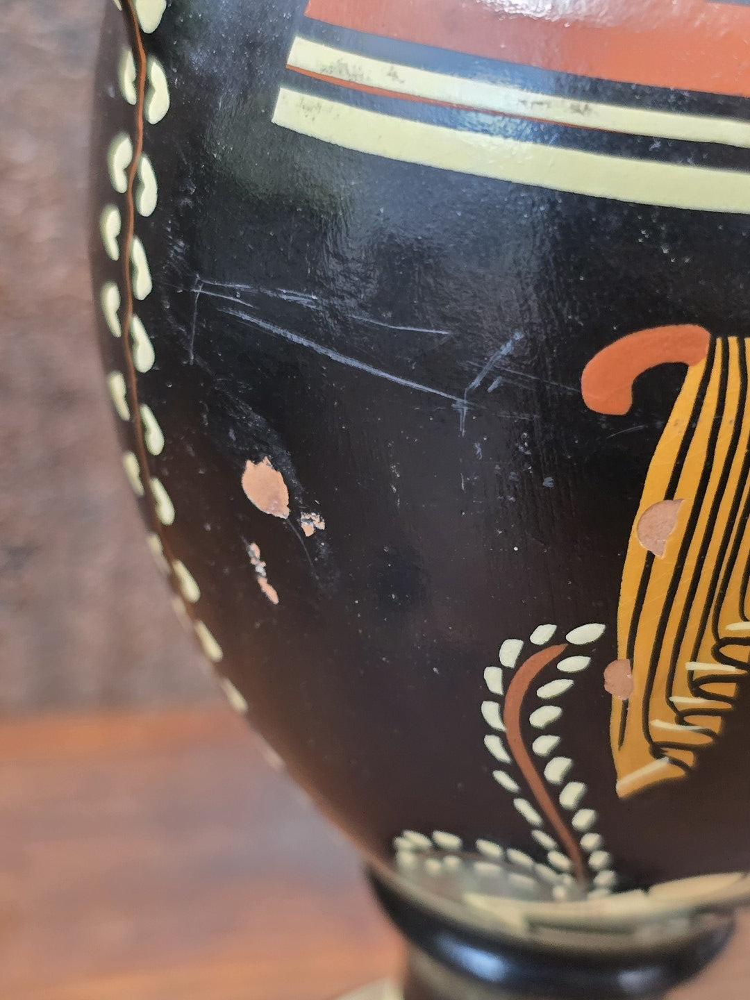 Griechische Keramikamphora mit sichtbaren Kratzern und Farbabplatzungen auf schwarzer Oberfläche in seitlicher Detailaufnahme