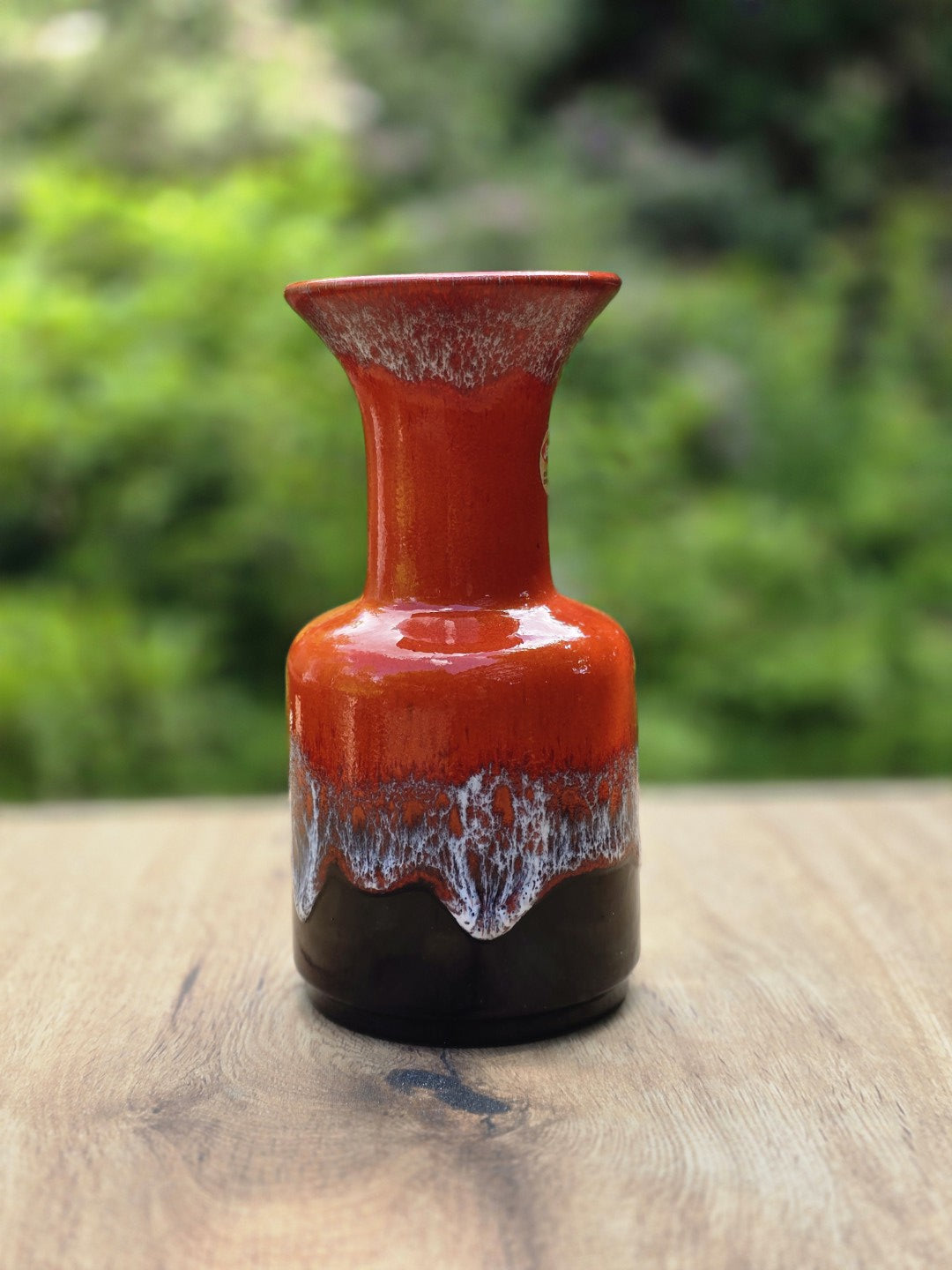 Rote Jasba Vase mit schwarzem Fuß, weißer Laufglasur und ausgestellter Öffnung auf Holztisch