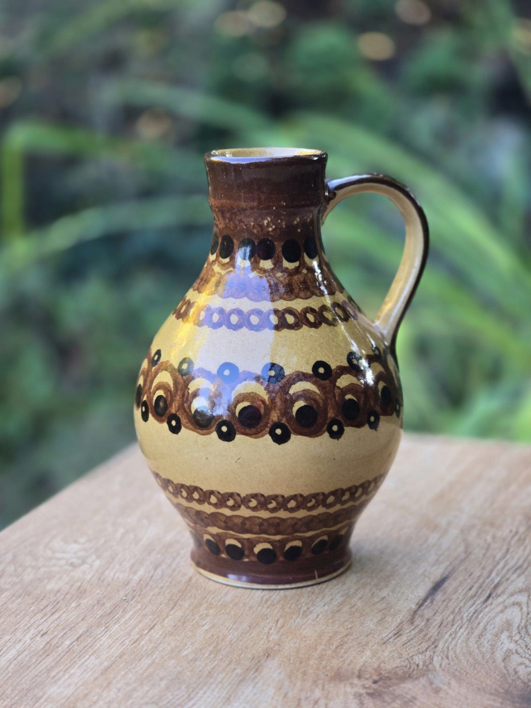 Vintage Keramik-Henkelkrug mit bauchiger Form und geometrischem Dekor in Ockergelb, Braun und Schwarz auf hellem Holztisch.