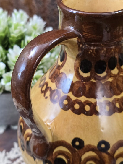Vintage Keramik-Henkelkrug mit handgemaltem Kreis- und Bogenmuster in Braun und Schwarz in naher Detailaufnahme des Korpus.