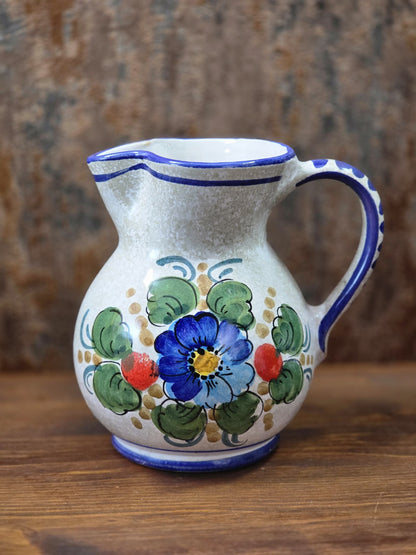 Vintage Keramik Krug mit blauem Blumendekor, grünen Blättern, rotem Akzent und blauem Rand auf Holztisch