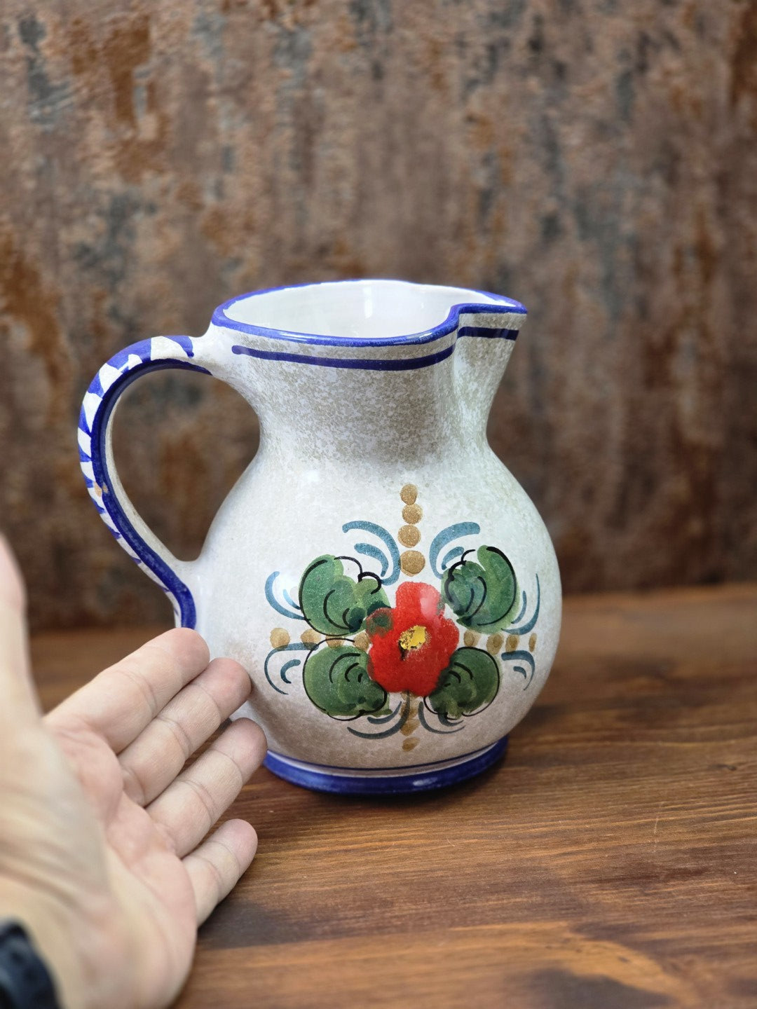 Vintage Keramik Krug mit roter Blume, grünem Blattdekor, blauem Henkel und Hand zum Größenvergleich