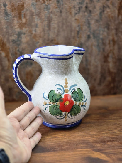 Vintage Keramik Krug mit roter Blume, grünem Blattdekor, blauem Henkel und Hand zum Größenvergleich