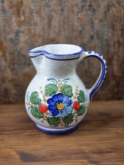 Vintage Keramik Krug mit blauer Blume, grünem Blattmuster, rotem Dekor und blauem Henkel auf Holztisch