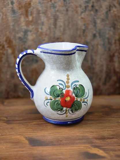 Vintage Keramik Krug mit rotem Blumendekor, grünen Blättern, blauem Rand und bauchiger Form auf Holztisch