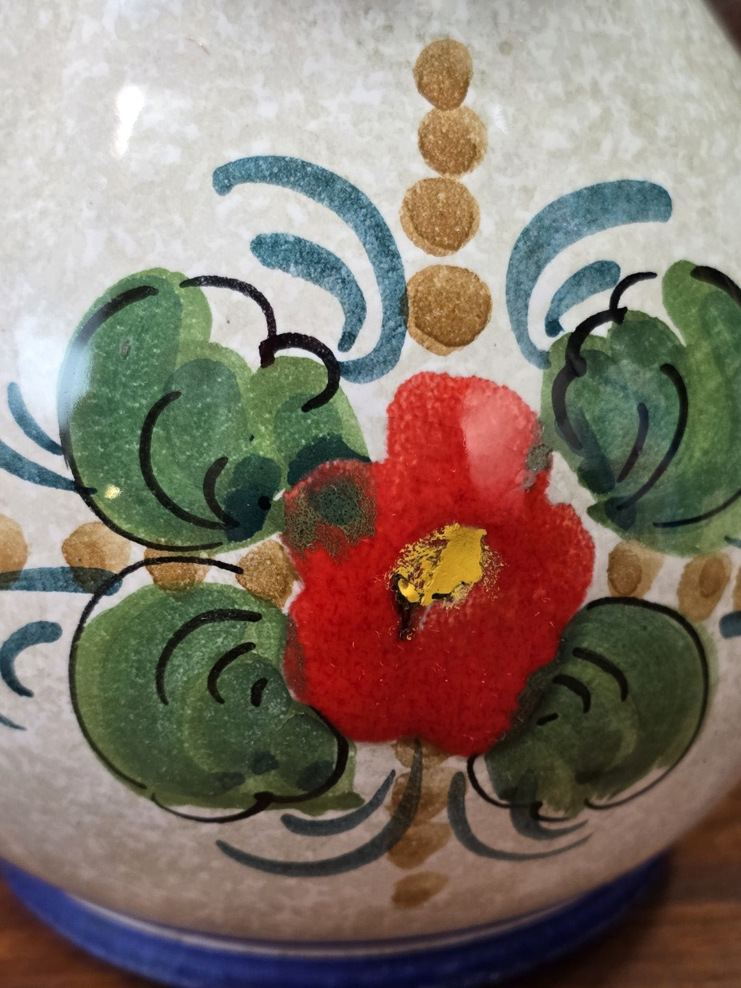 Vintage Keramik Krug im Detail mit roter Blume, grünen Blättern, blauen Schwüngen und gesprenkelter Glasur