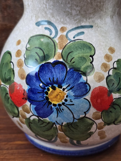 Vintage Keramik Krug im Detail mit blauer Blume, grünen Blättern, roten Akzenten und glänzender Glasur
