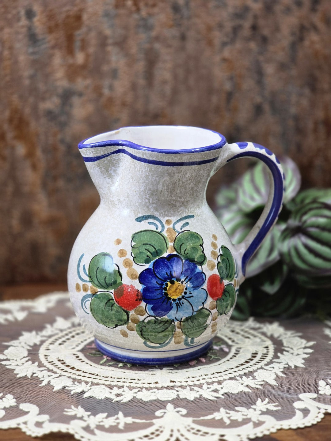 Vintage Keramik Krug mit blauem Blumendekor, bauchiger Form, blauem Henkel und Spitze im Hintergrund