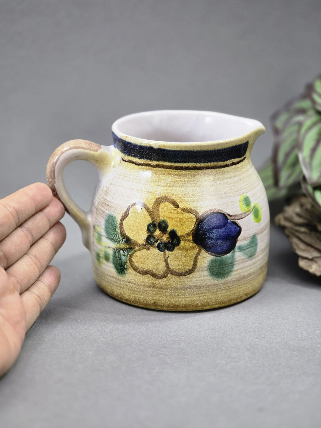 Vintage Milchkännchen aus Keramik mit floralem Muster, Henkel und hellem Grundton neben einer Hand zum Größenvergleich