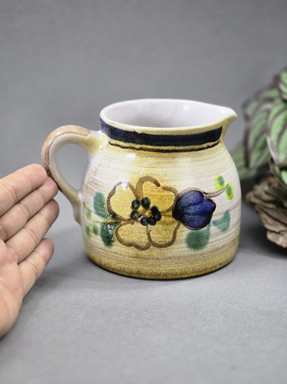 Vintage Milchkännchen aus Keramik mit floralem Muster, Henkel und hellem Grundton neben einer Hand zum Größenvergleich