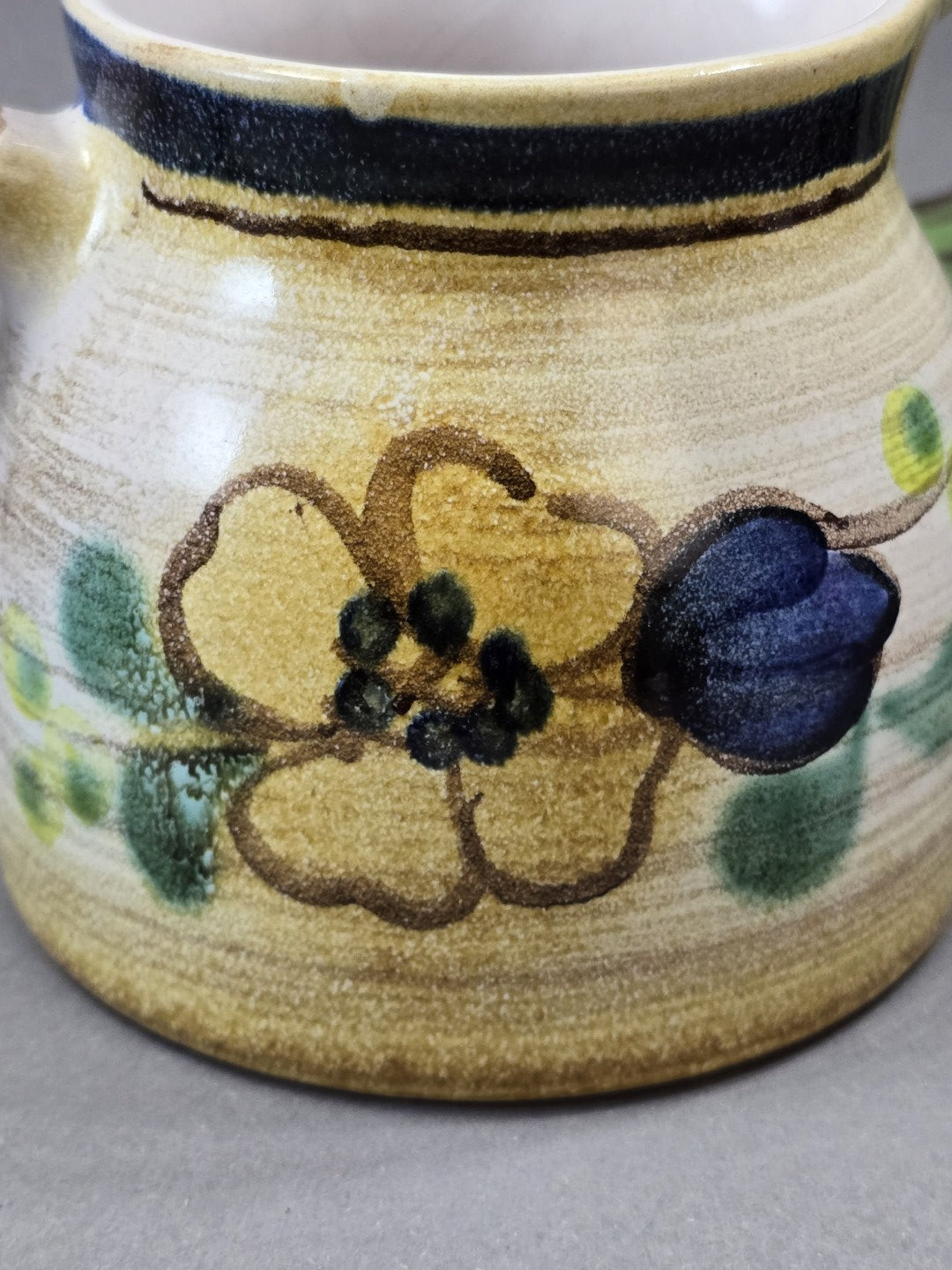 Detail des Blumenmotivs mit gelber Blüte, dunkelblauer Knospe und grünem Dekor auf heller Keramikglasur